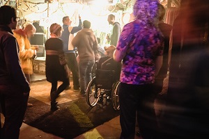 Partyszene mit Menschen, eine Person nutzt einen Rollstuhl.
